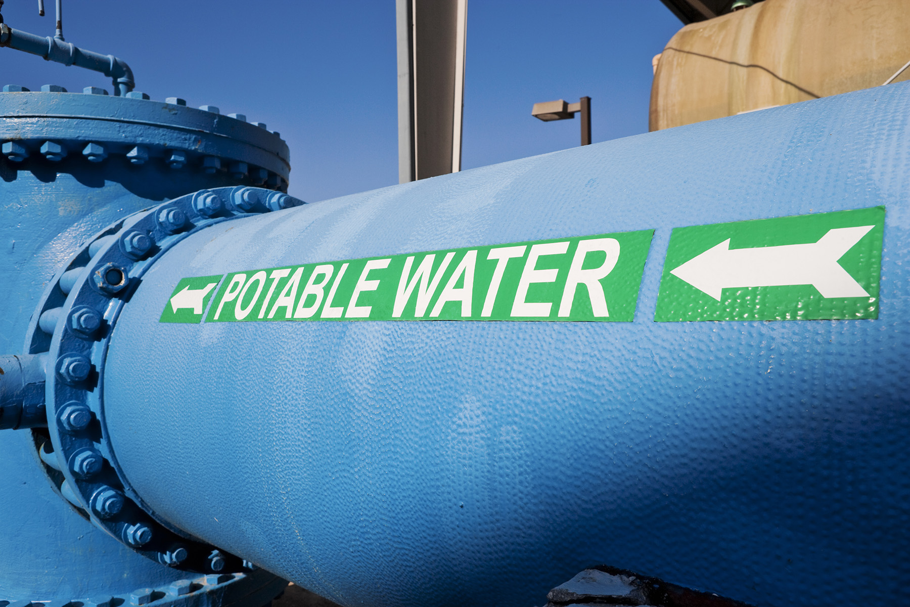 Photograph shows a close-up view of a large water pipe. The words “potable water” are written in white on the pipe.