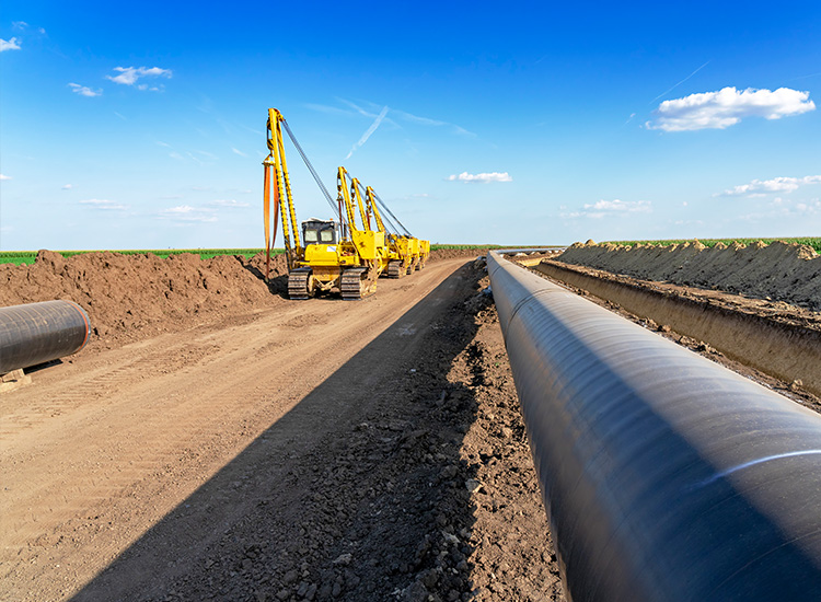 Picture shows a large-diameter pipe in the soil. To the left are three tractors used to dig out the earth. 
