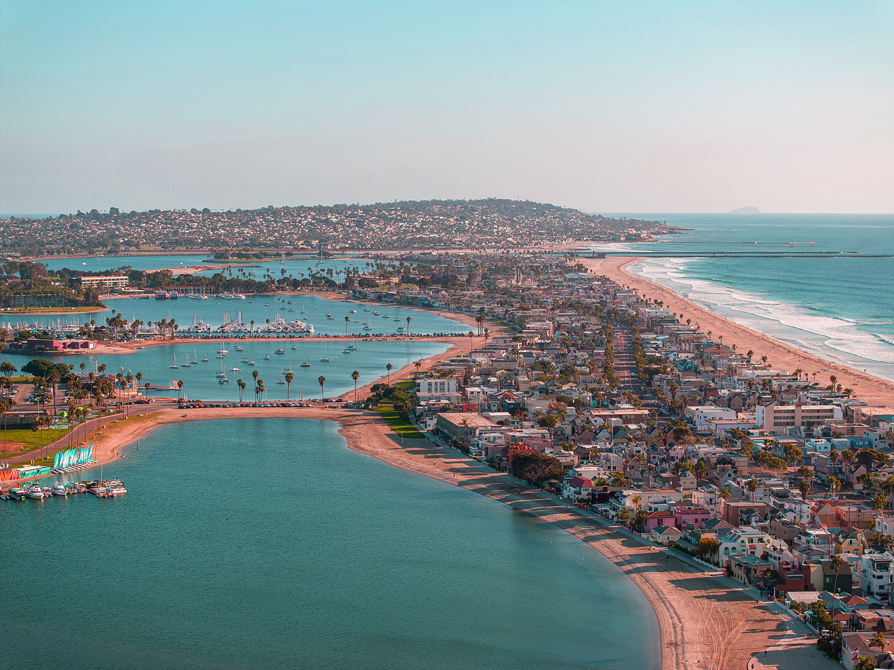 An aerial photograph shows coastal San Diego with a multitude of homes, commercial buildings, boats, as well as beachfront and water. 