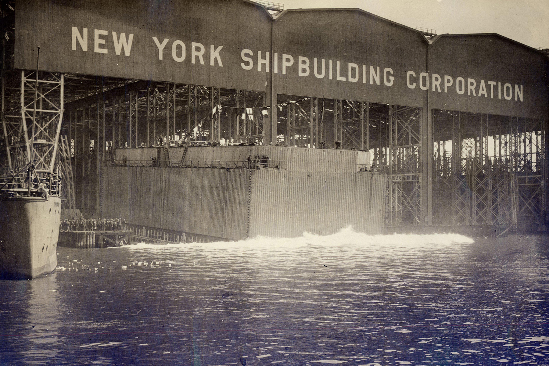 Photograph shows a large wooden structure being launched into the water.