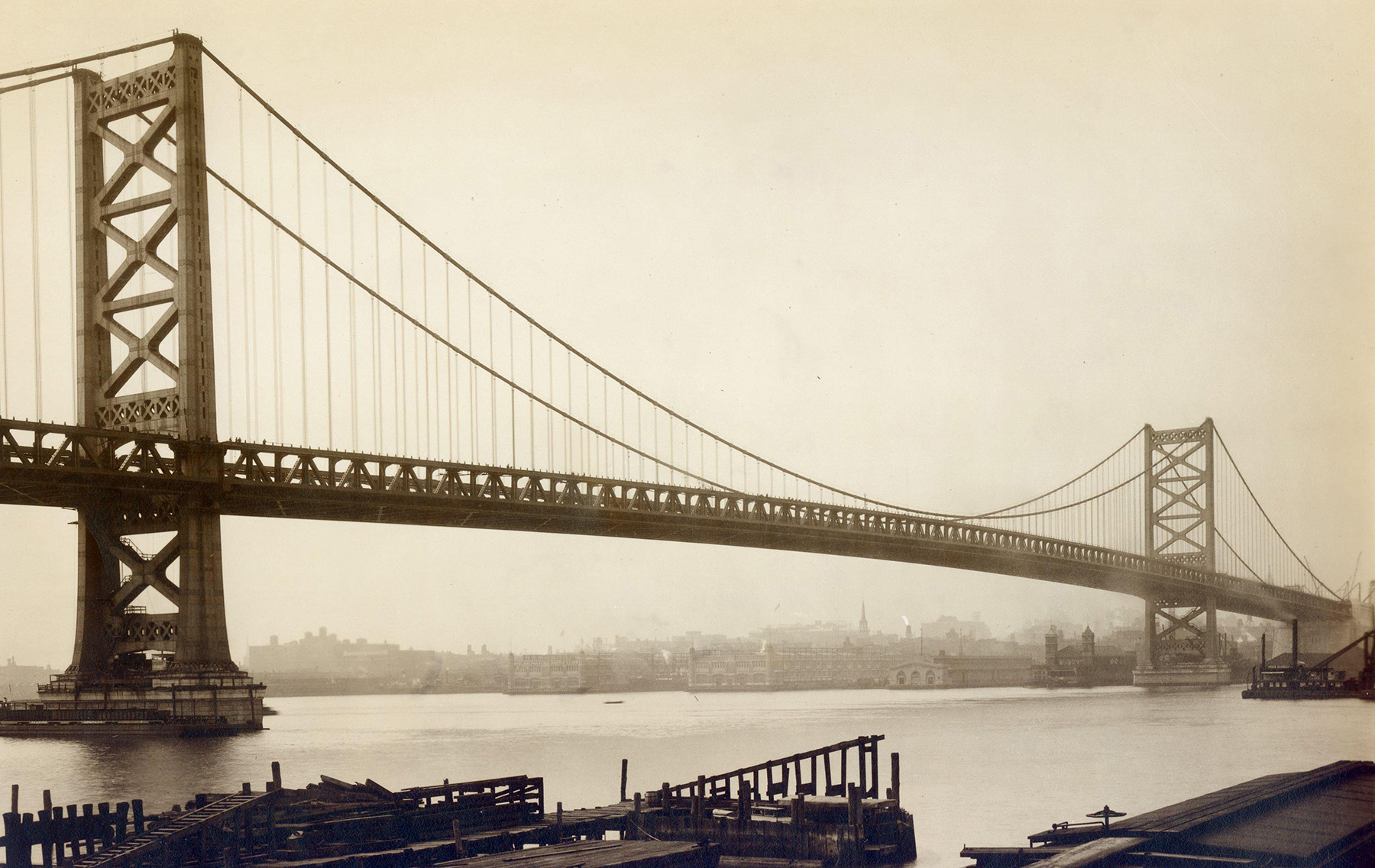 The picture shows the main span of a bridge along with its two piers. A city can be seen faintly in the distance. 