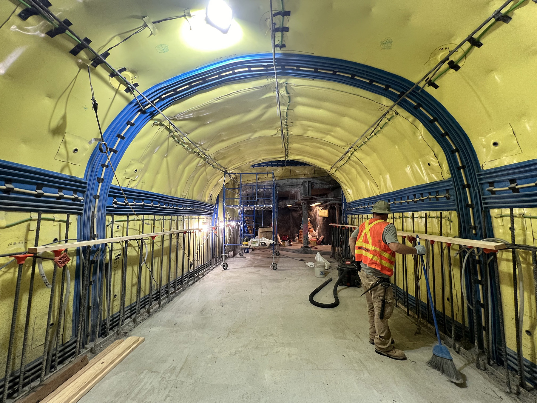 A finished concrete floor and completed archway are visible. Bright yellow waterproofing material covers the arch ceiling and walls.