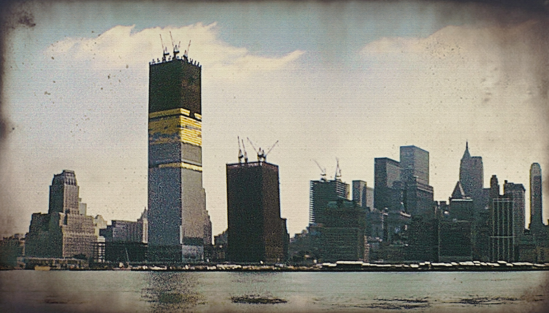 Photograph shows two supertall buildings under construction. On top of both buildings are cranes that help lift heavy steel into place.
