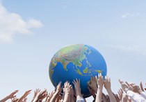 Hands hold up a ball that has the continents on it.