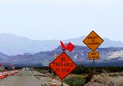 Highway in desert with traffic cones and signs saying ‘Be prepared to stop’ and ‘Subject to Flooding’