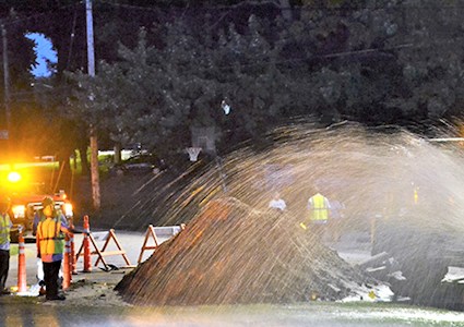 Workers repairing a water main break, with water spraying from main
