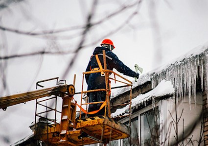 A worker on a crane knocking down huge icicles