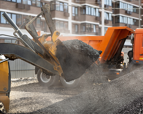 Excavator bucket set to pour hot asphalt onto a road