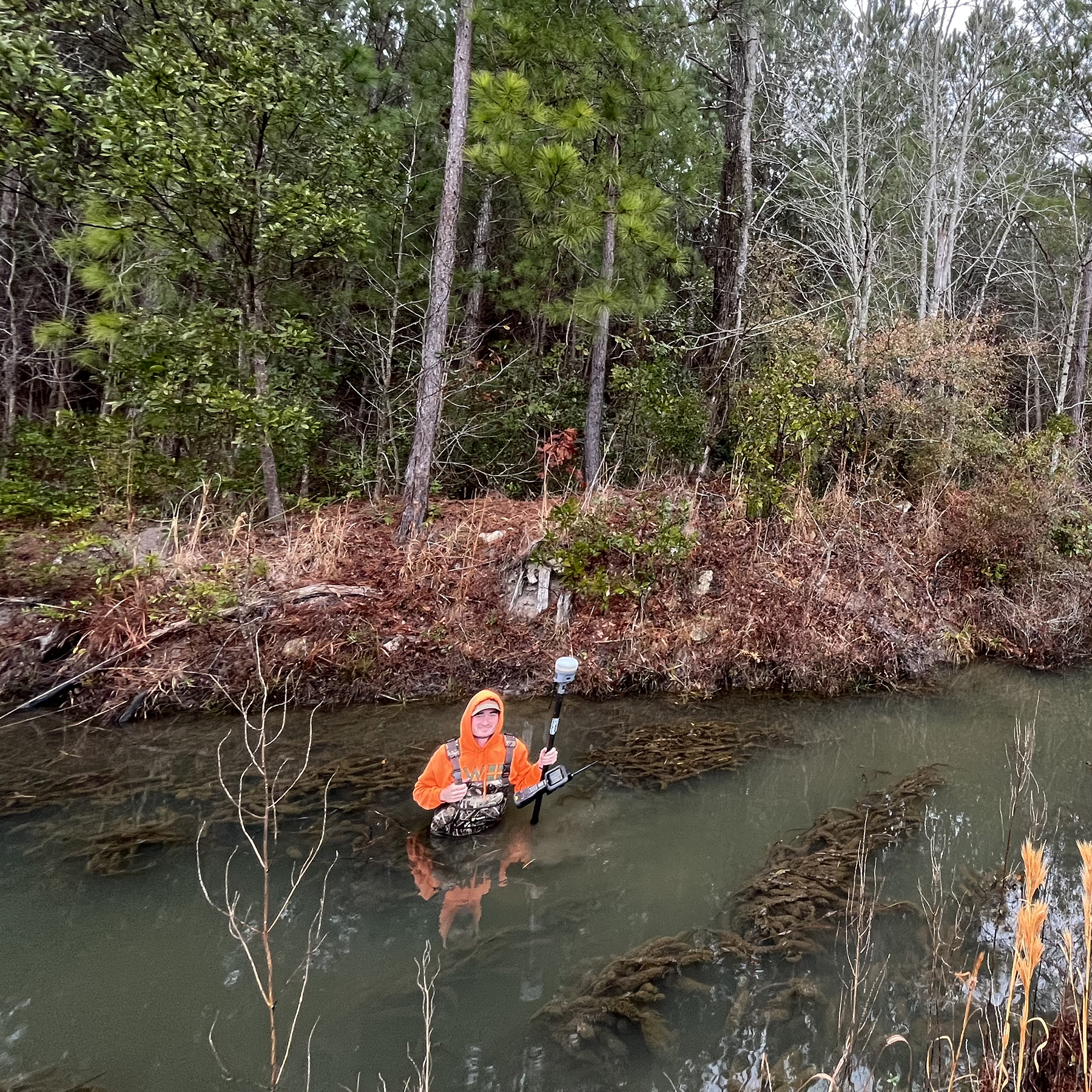 a person stands waist-deep in water with surveying equipment