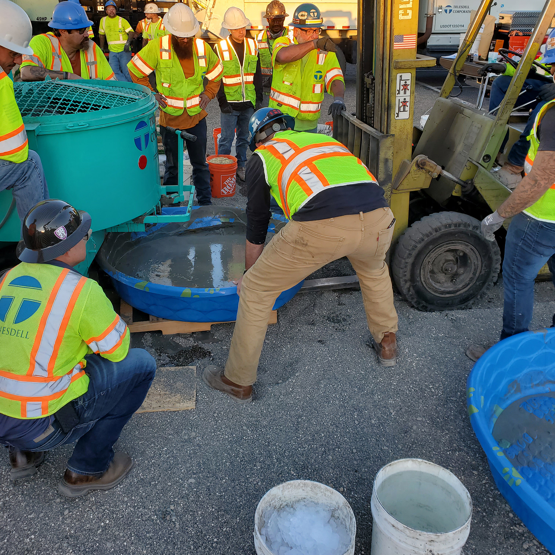 workers in hardhats and green work vests work with concrete