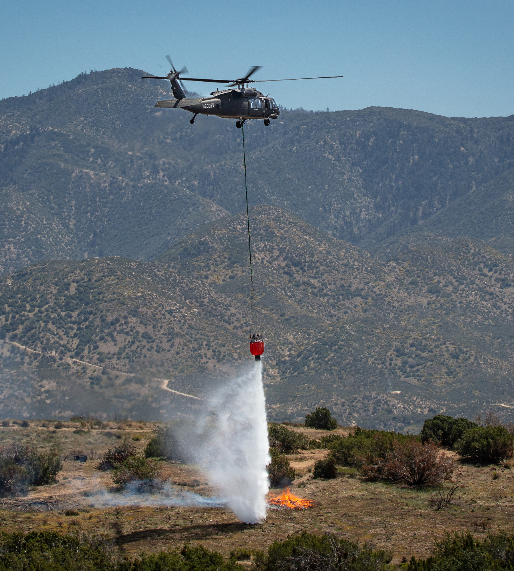 a helicopter dangles a fire-suppression device above a fire in a tree-heavy area a helicopter dangles a fire-suppression device above a fire in a tree-heavy area