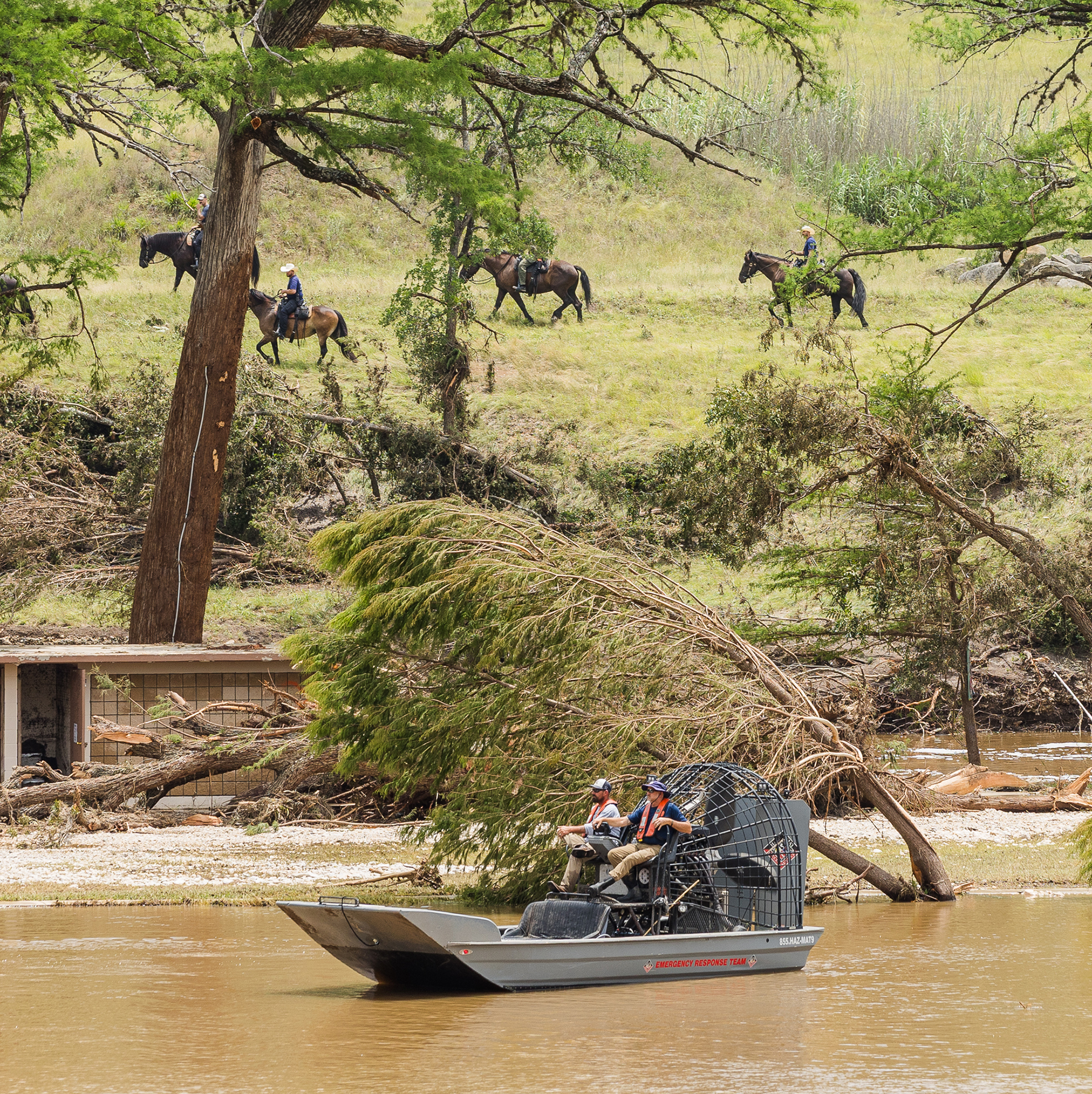 people travel across water via airboat amid sagging trees and people on horseback in the background