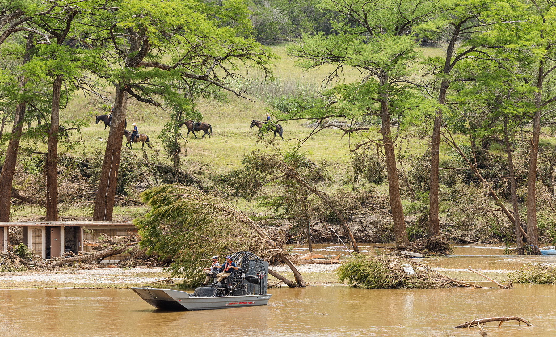 people travel across water via airboat with sagging trees and people on horseback in the background people travel across water via airboat with sagging trees and people on horseback in the background
