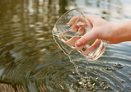 Hand holding clear glass that has scooped water out of a pool or pond.