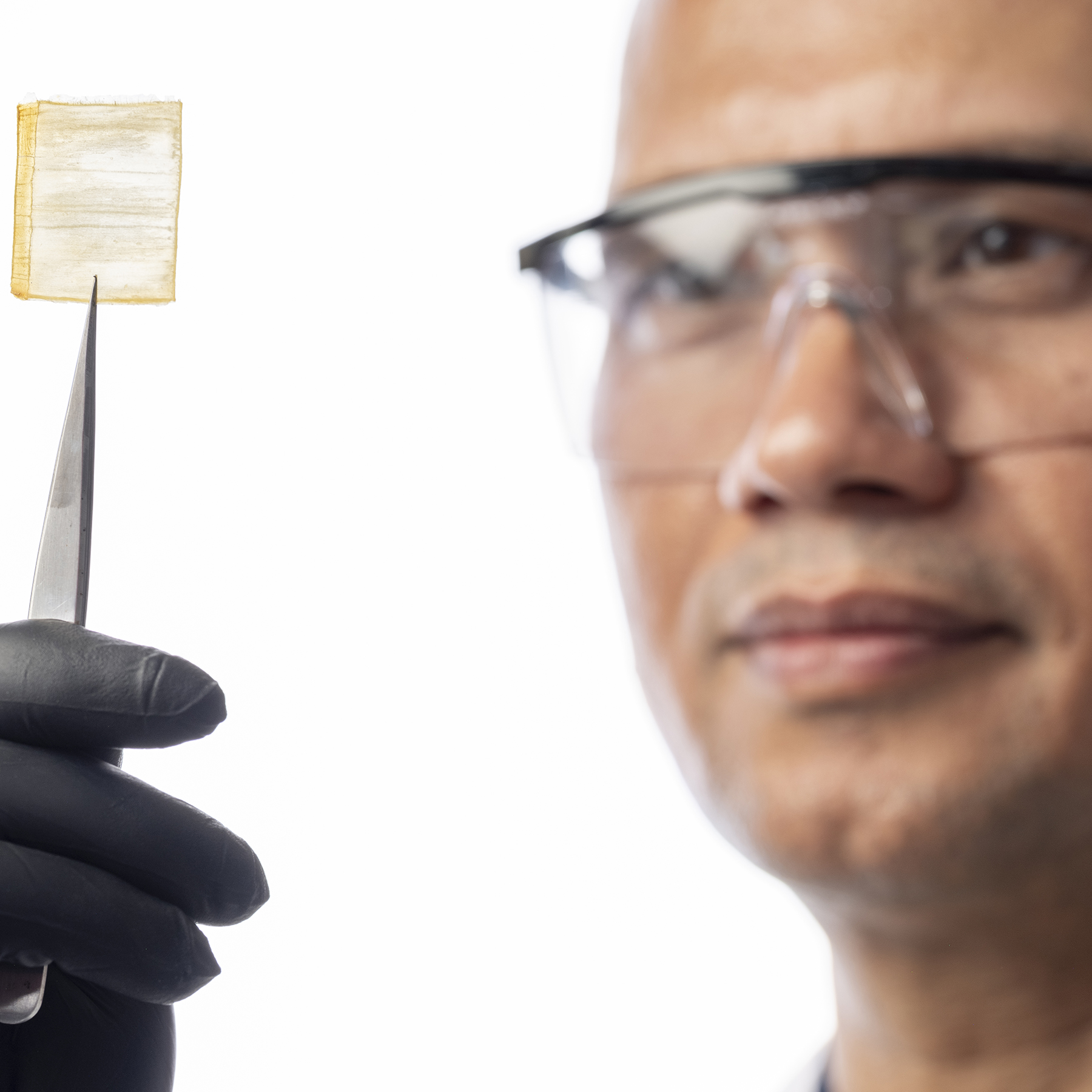 a man wearing goggles holds up a square-shaped wood object with a sharp metal instrument