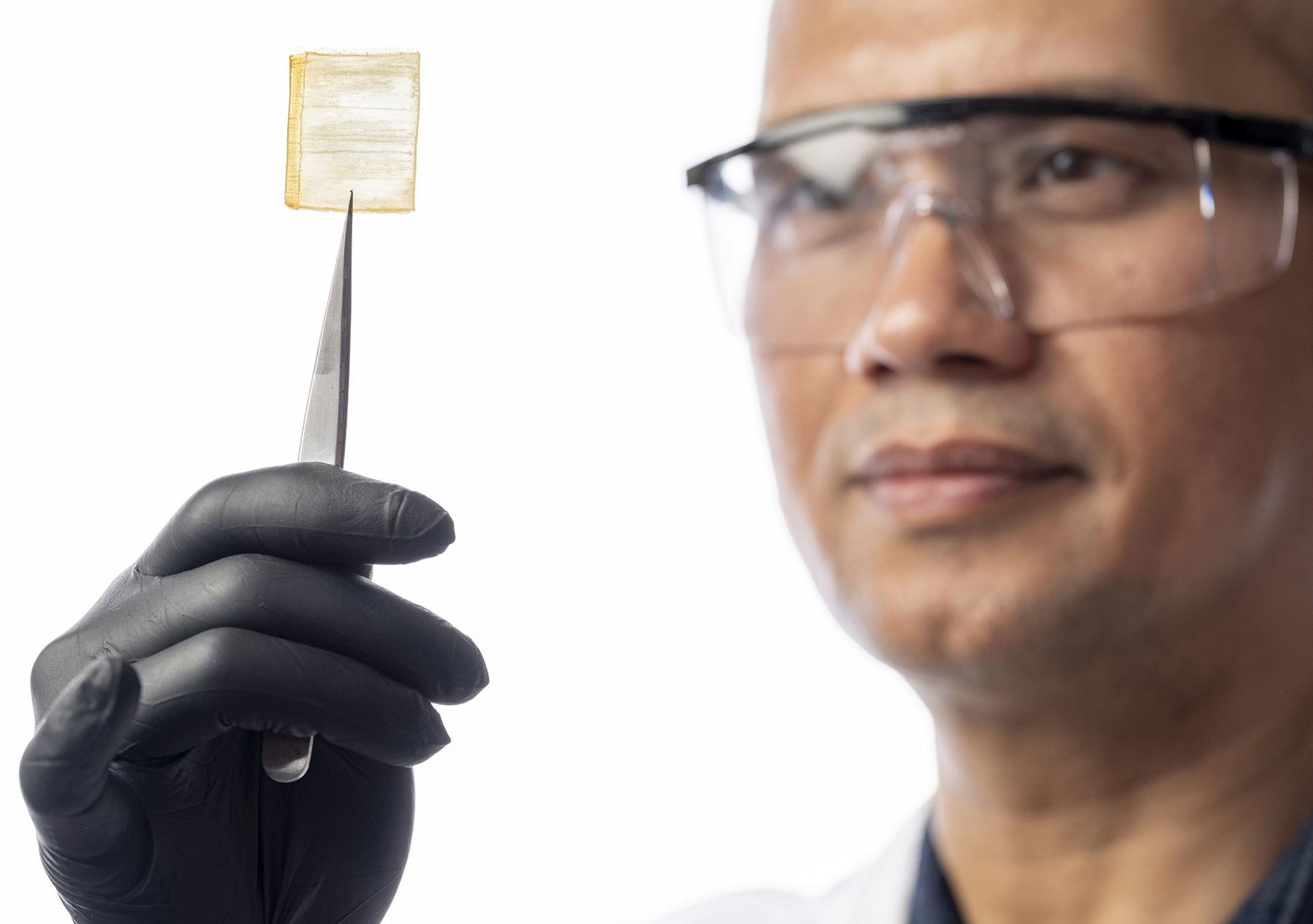 man with goggles holds up a square-shaped piece of wood with a sharp instrument