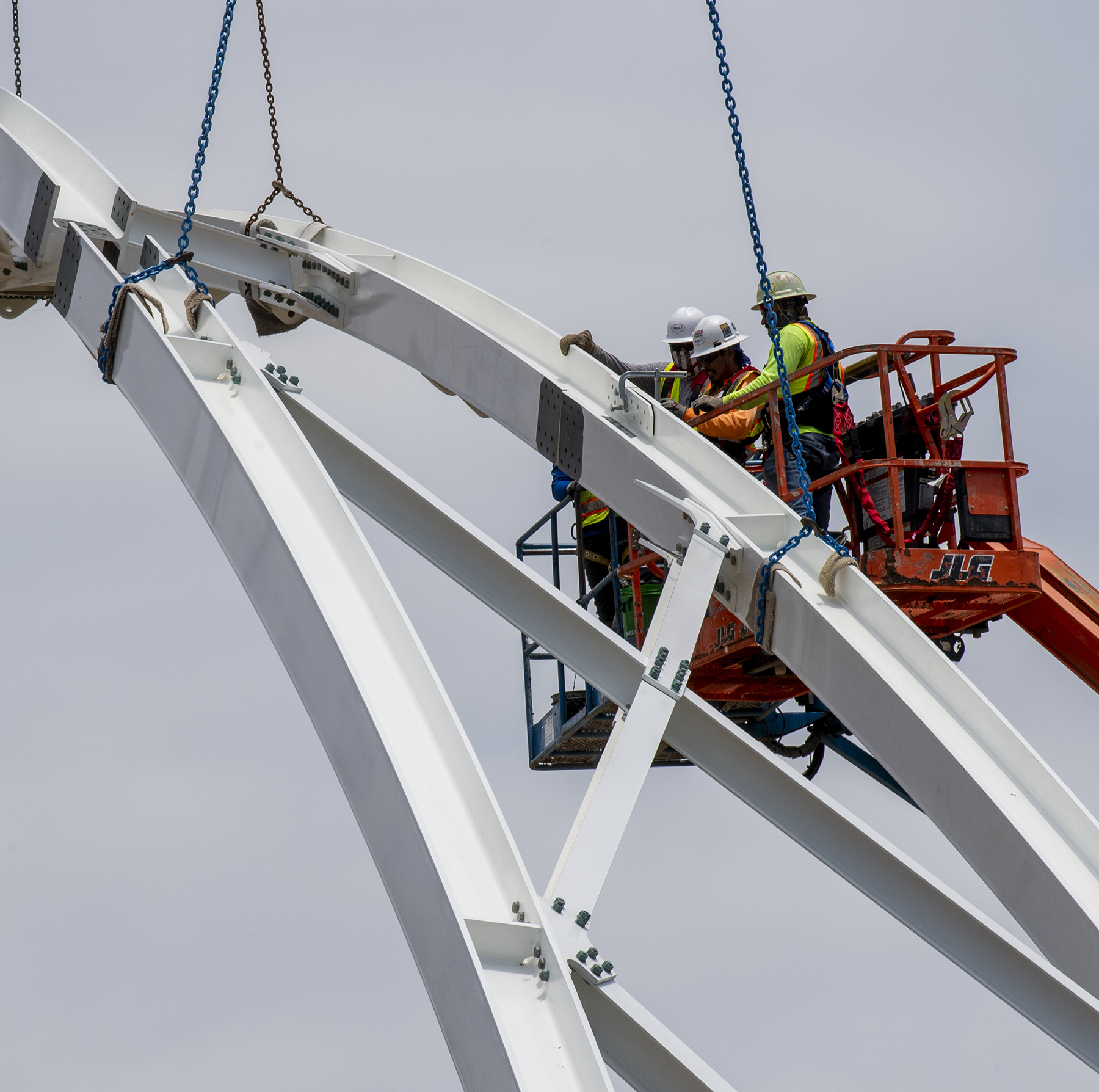 people in a cherry picker work on the arch of a pedestrian bridge