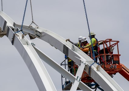 people in a cherry picker work on the arch of a pedestrian bridge
