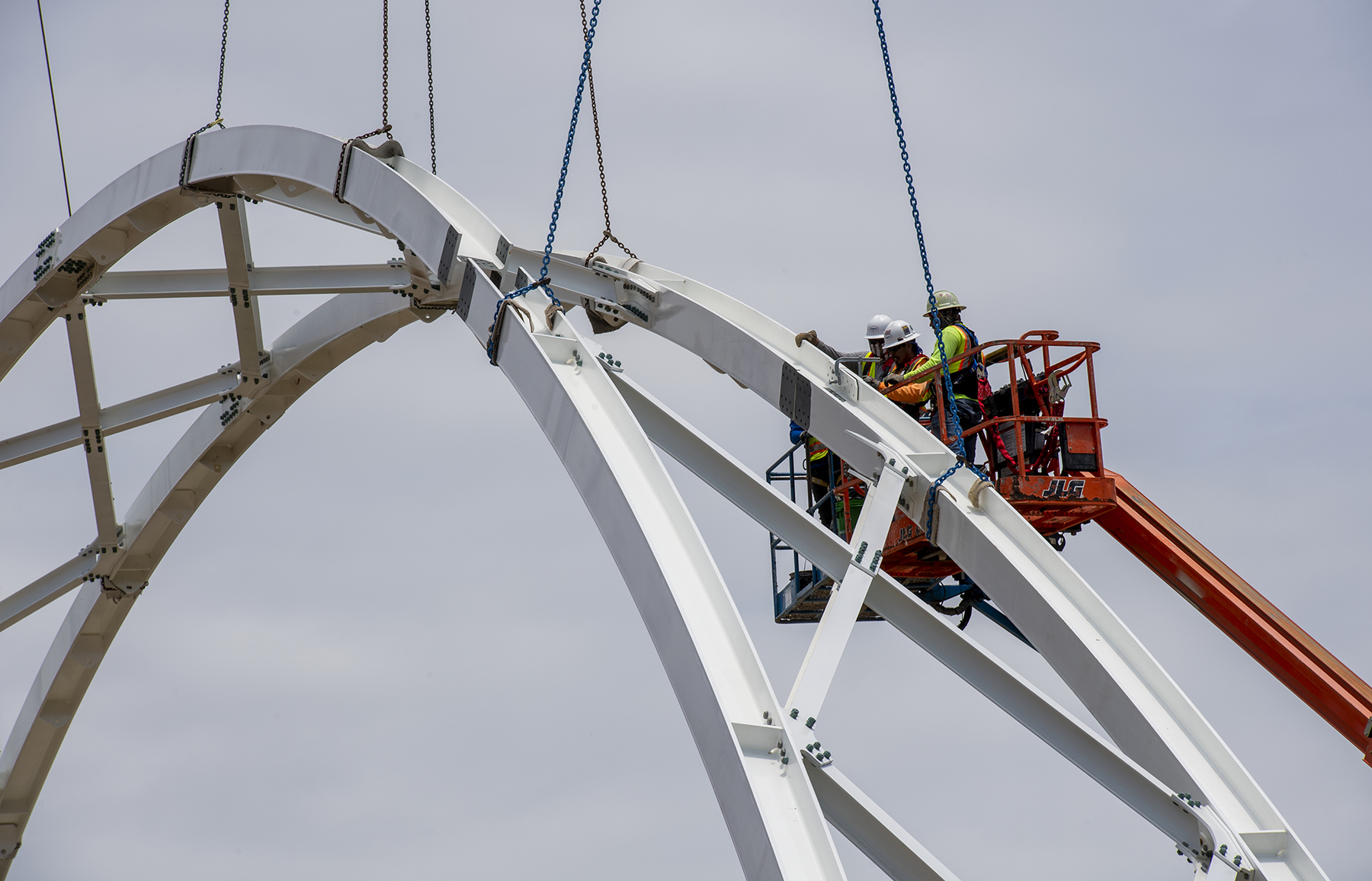 a crew works on an arching portion of the pedestrian bridge a crew works on an arching portion of the pedestrian bridge