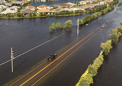 A coastal road partially submerged by flooding with a vehicle that can't get through