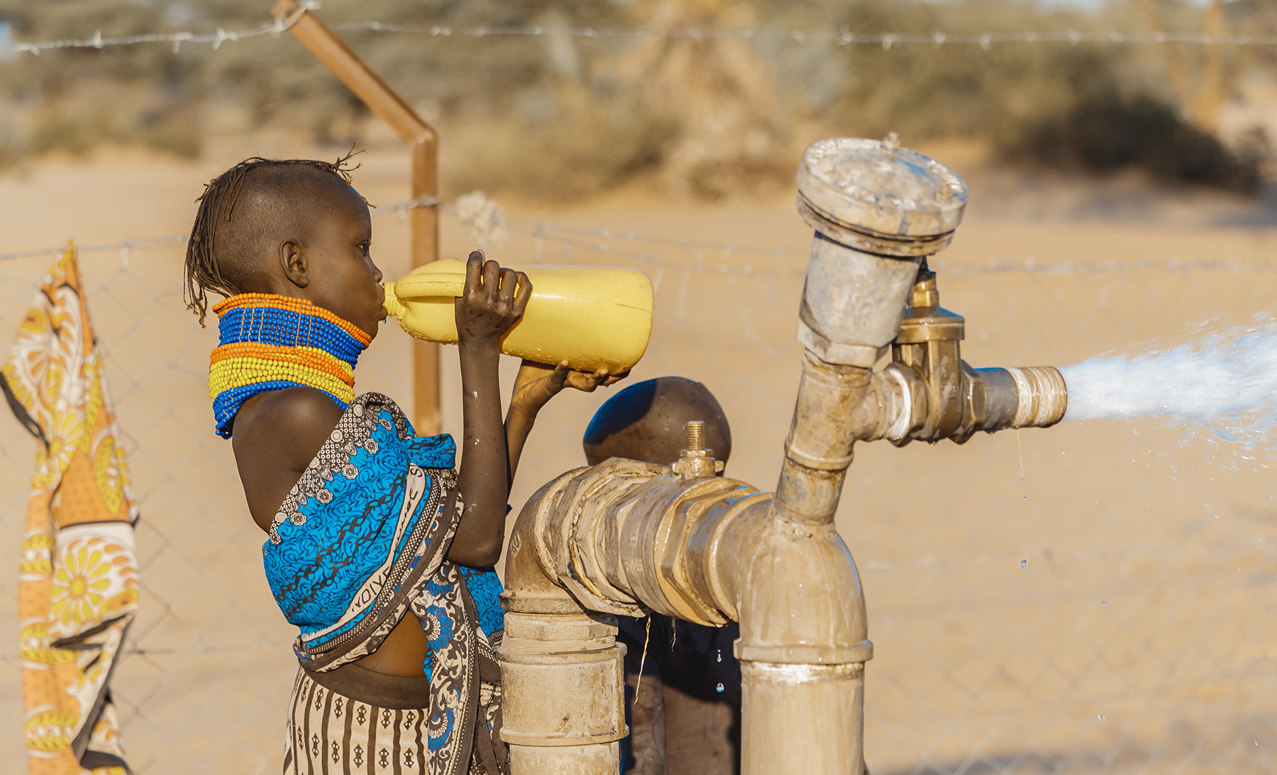 a child drinks from a yellow bottle as water flows from a waterworks a child drinks from a yellow bottle as water flows from a waterworks