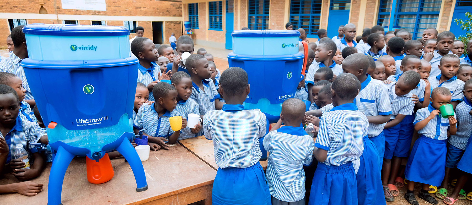 children dressed in blue gather around an outdoor table with water dispensers children dressed in blue gather around an outdoor table with water dispensers