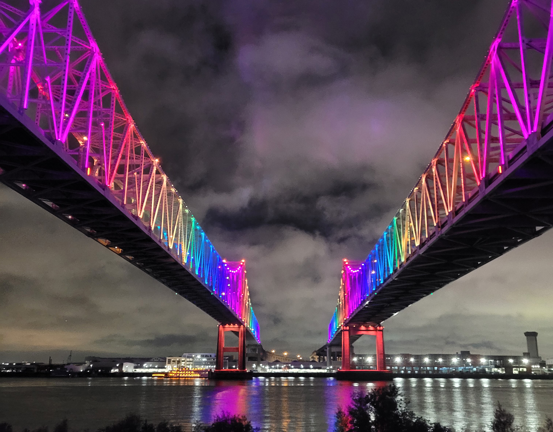 a twin-span bridge is lit up in rainbow colors under a night sky a twin-span bridge is lit up in rainbow colors under a night sky