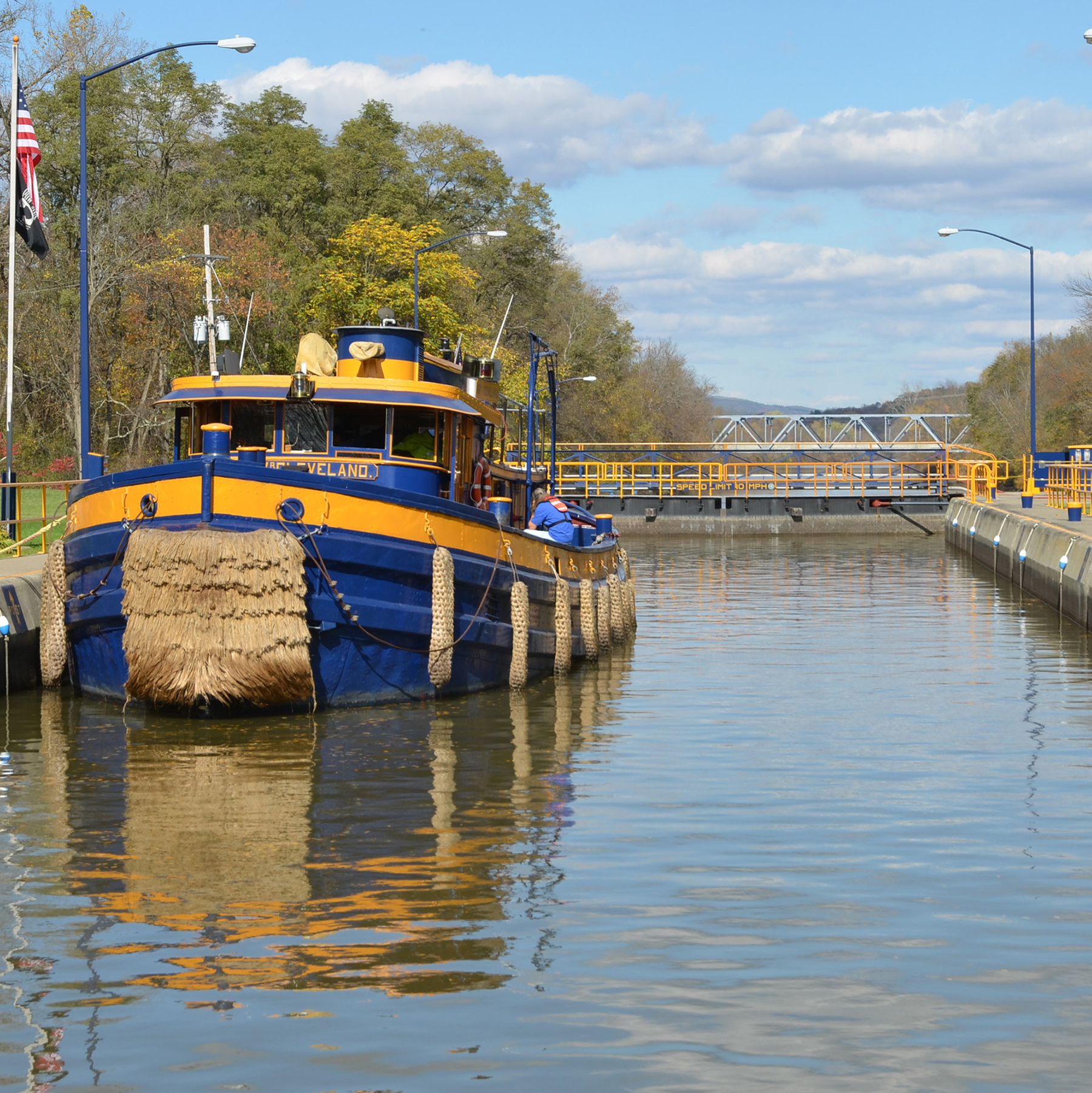 a blue and yellow tugboat sits in a lock of the Erie Canal