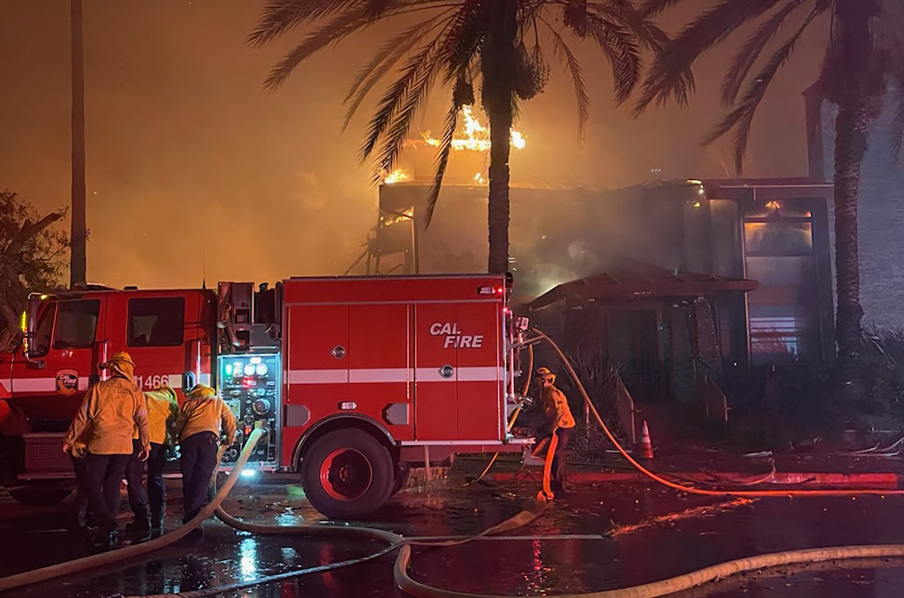 firefighters near a fire truck prepare as a fire burns in the background