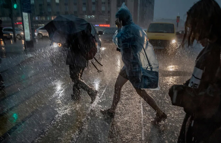 People crossing a very rainy street with headlights shining