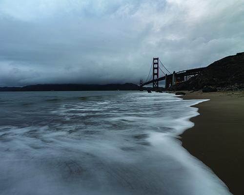 Water flowing onto beach on a cloudy day with Golden Gate Bridge in background