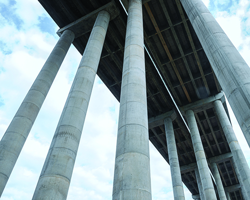 Close up of three bridge columns from below, looking up at bridge structure
