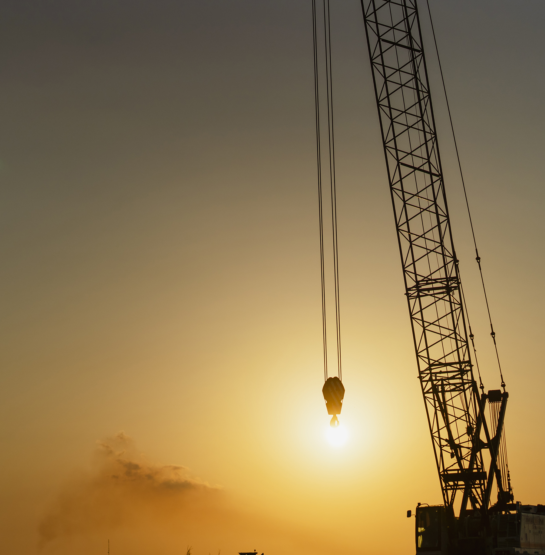 cranes work with the sun on the horizon in the background