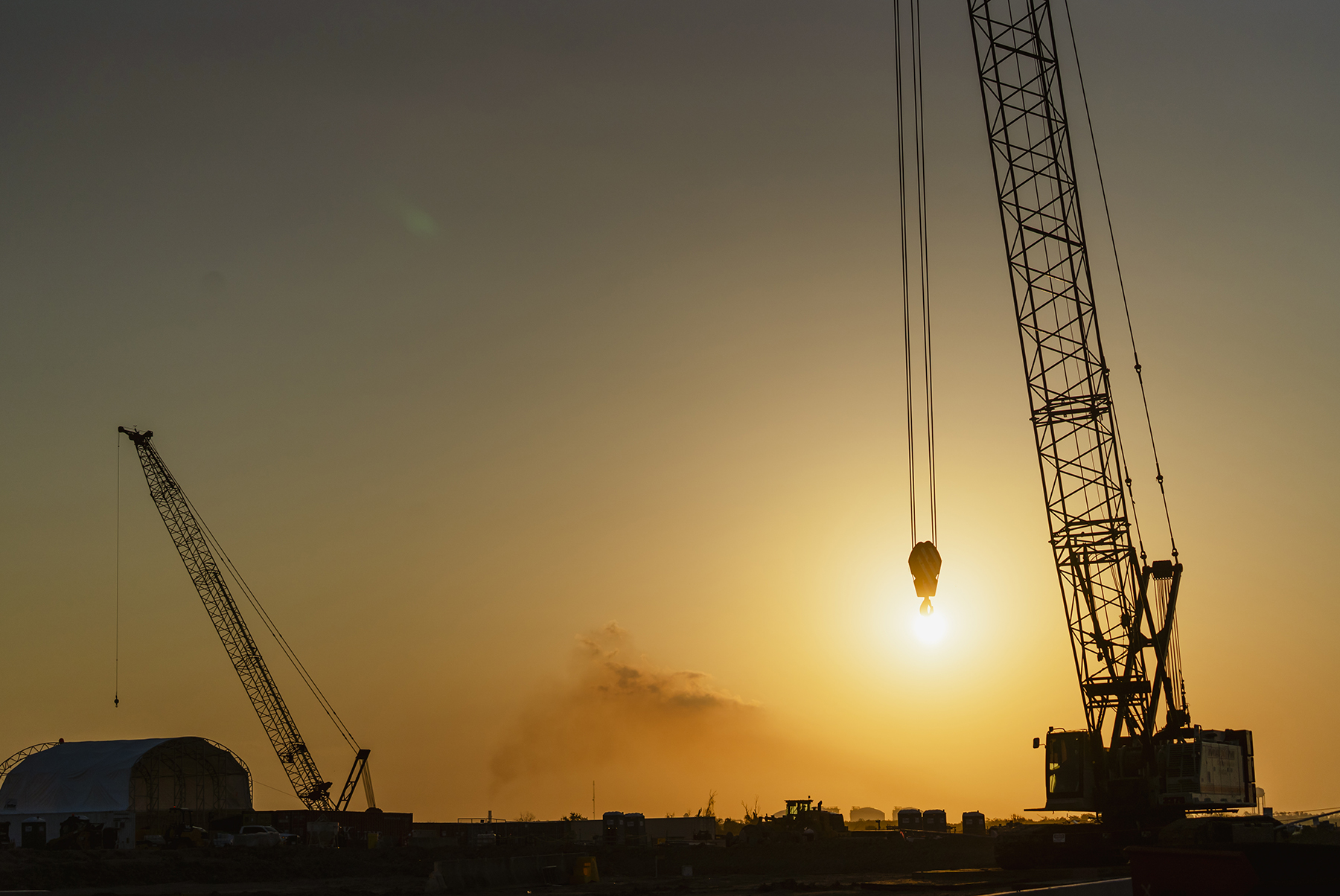 cranes work with the sun on the horizon in the background