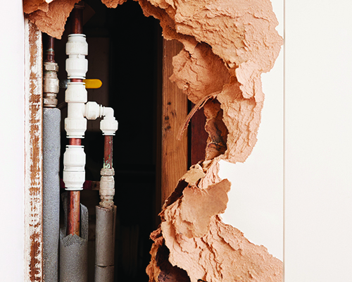 Damaged wall exposing burst water pipes