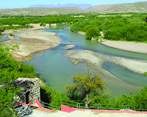 Rio Grand River between Mexico and the USA, steps in foreground, with greenery on either side of the river