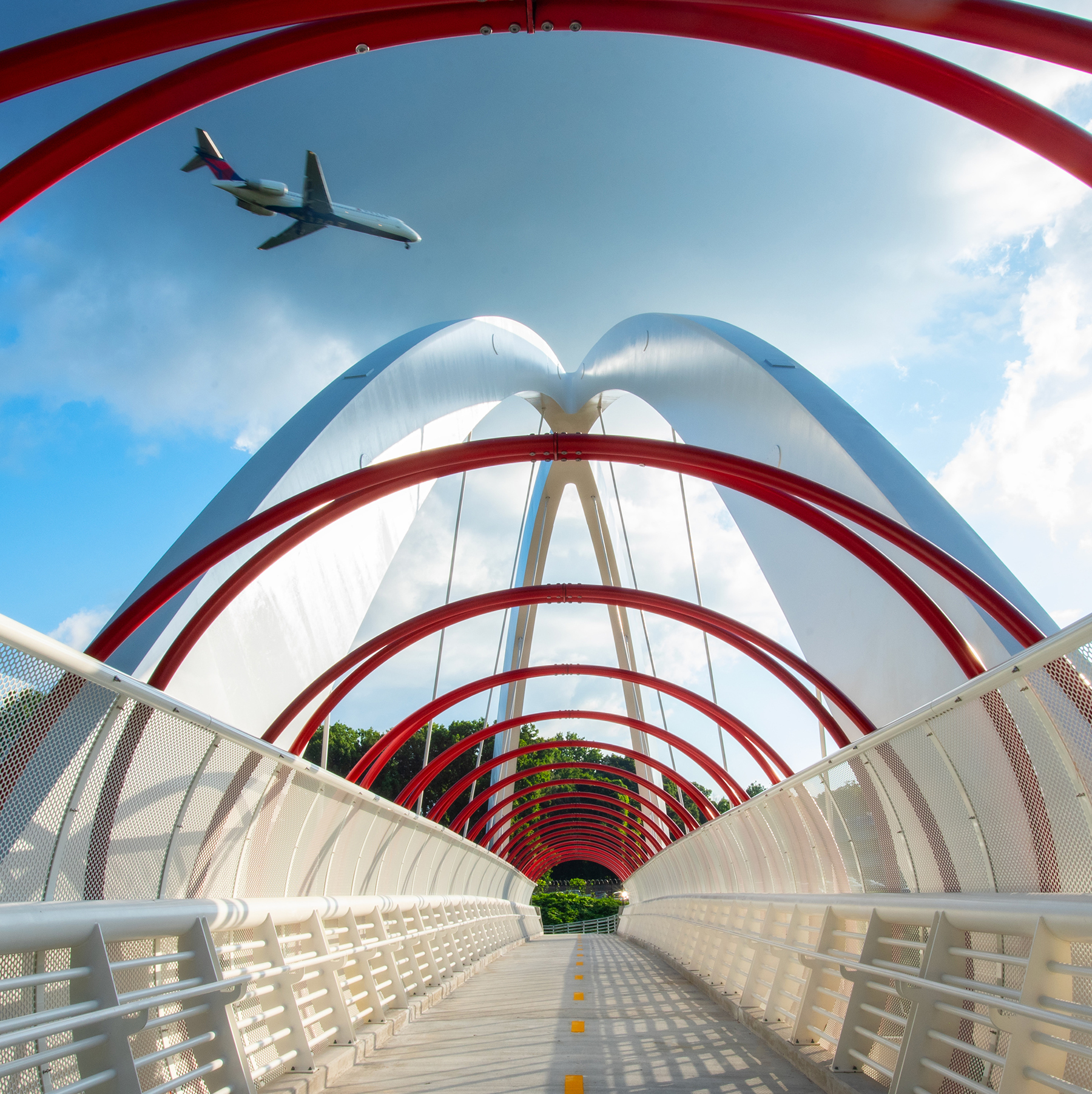 an airplane flies over a red and white pedestrian bridge