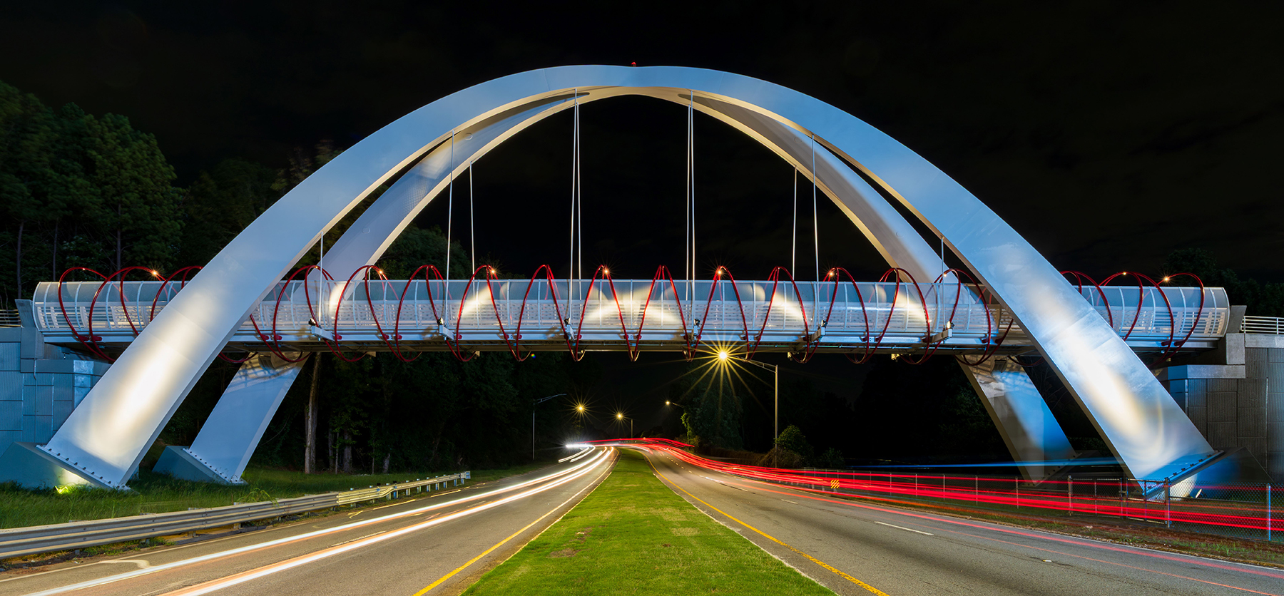 a white and red bridge stretches across a roadway under the night sky