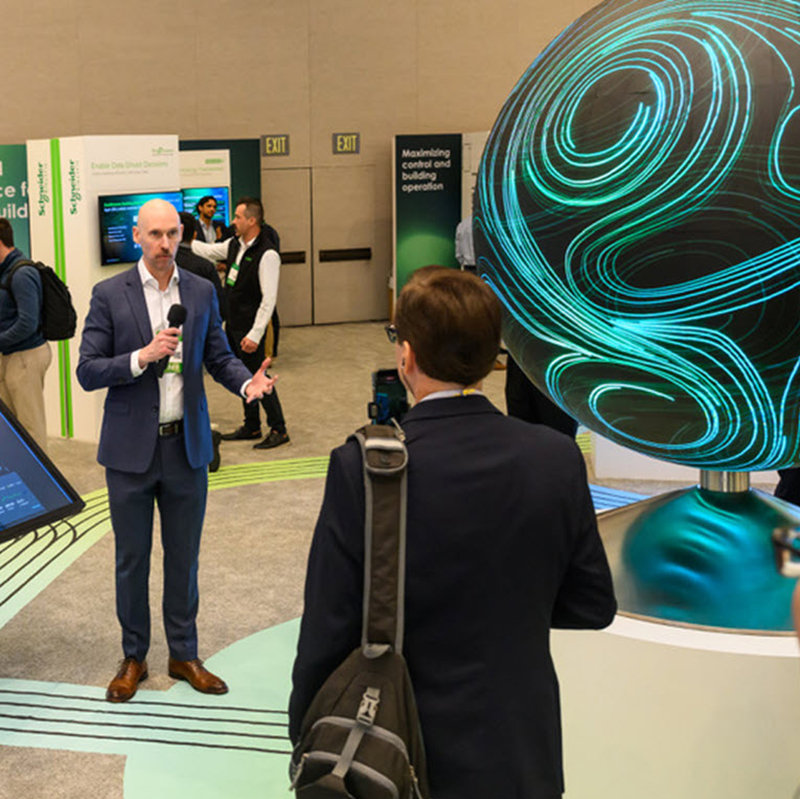 a person speaks into a microphone in a crowded room with a sphere-like object on the right side of the frame