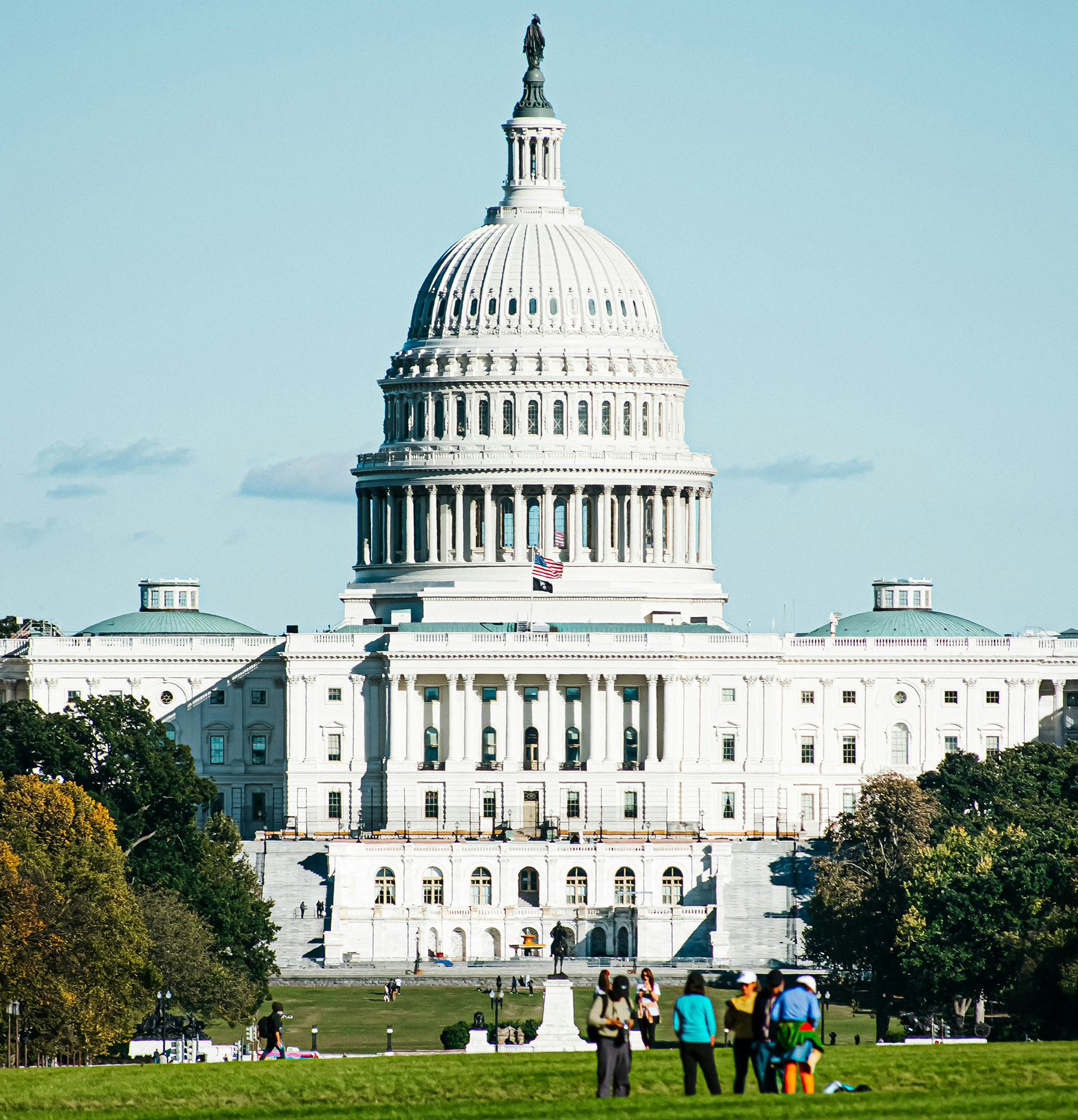 image of the U.S. Capitol with people standing on the lush green lawn