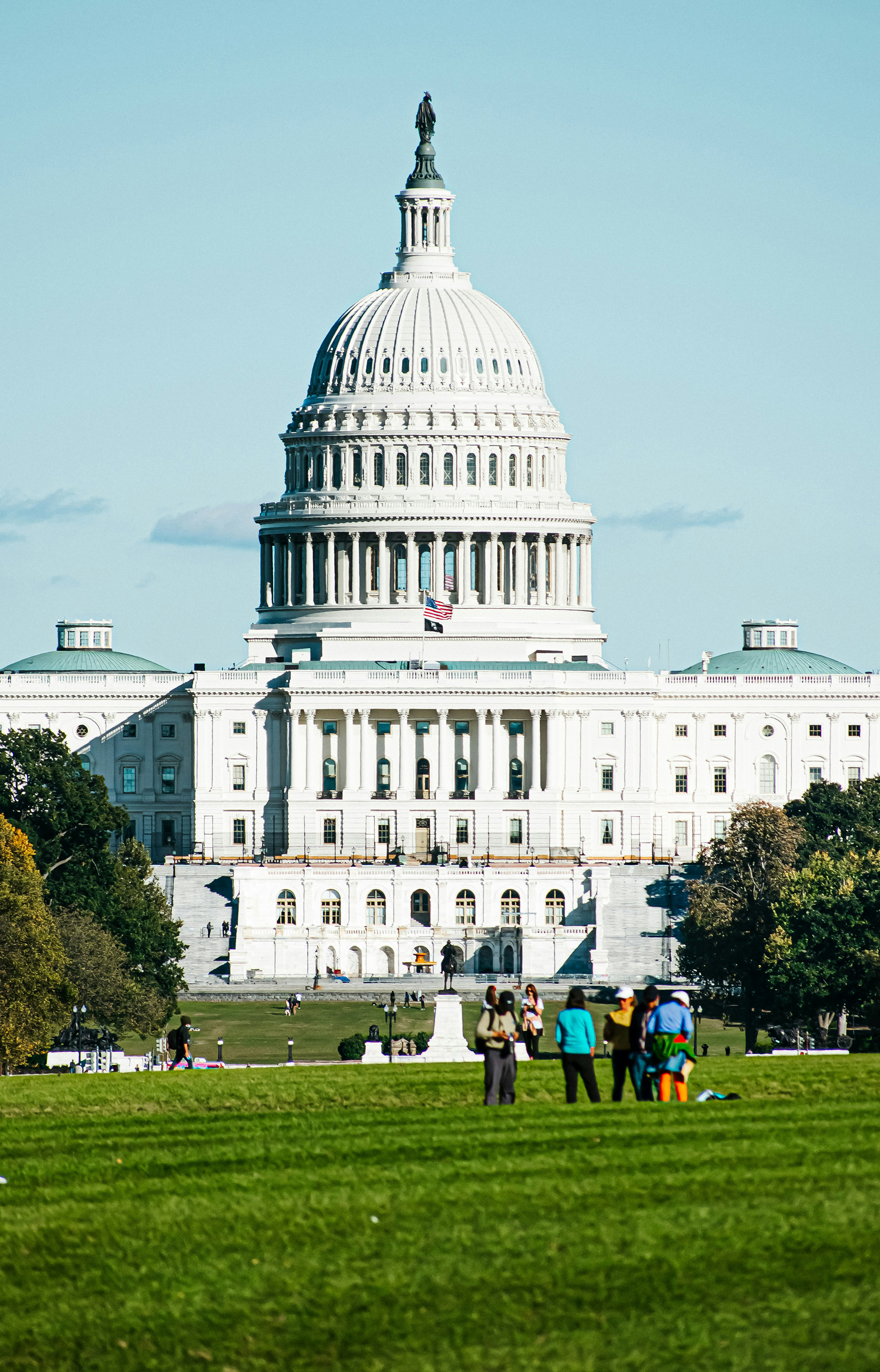 image of the U.S. Capitol with people standing on the lush, green lawn