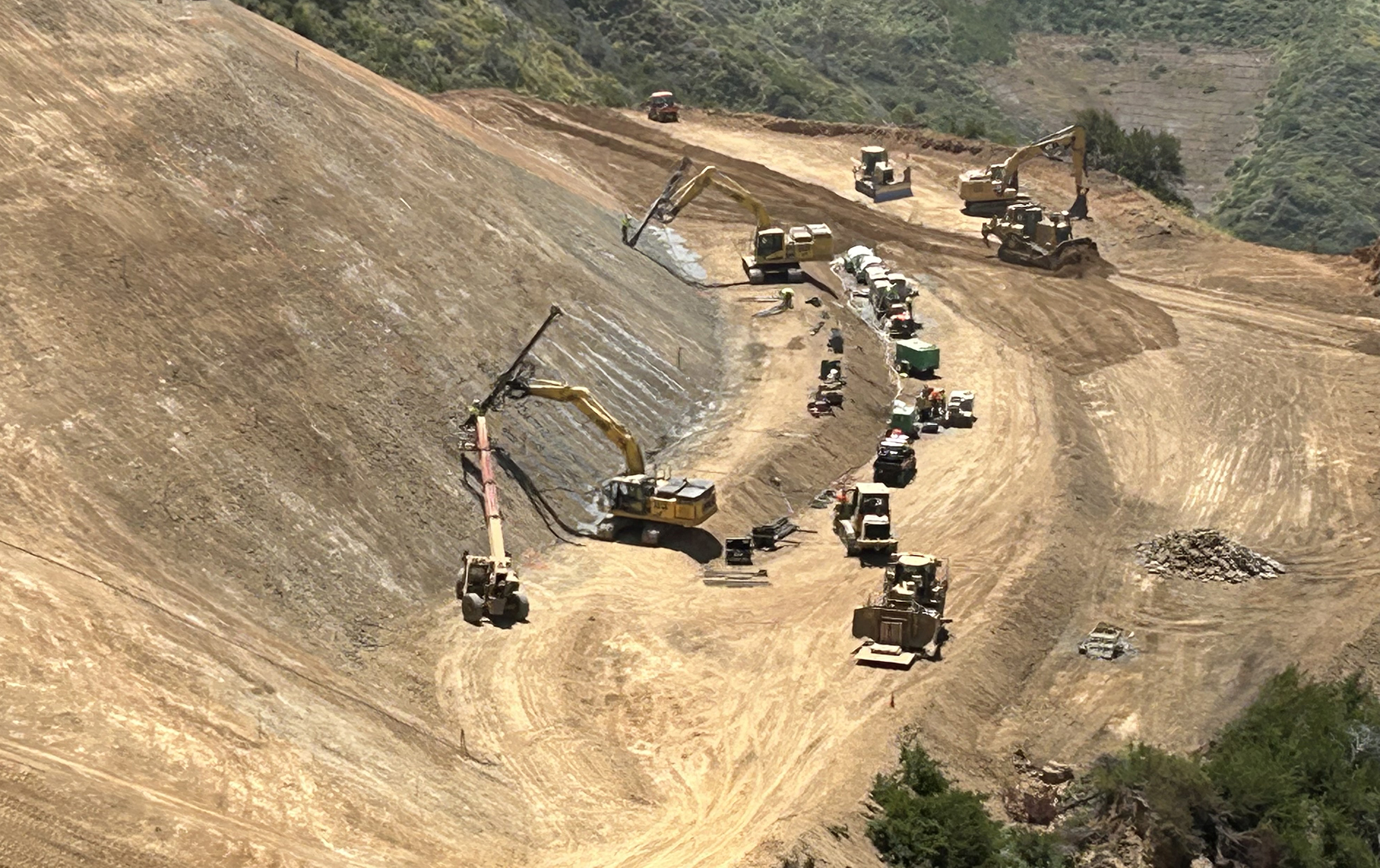 Excavators and vehicles working along terraced landslide bench
