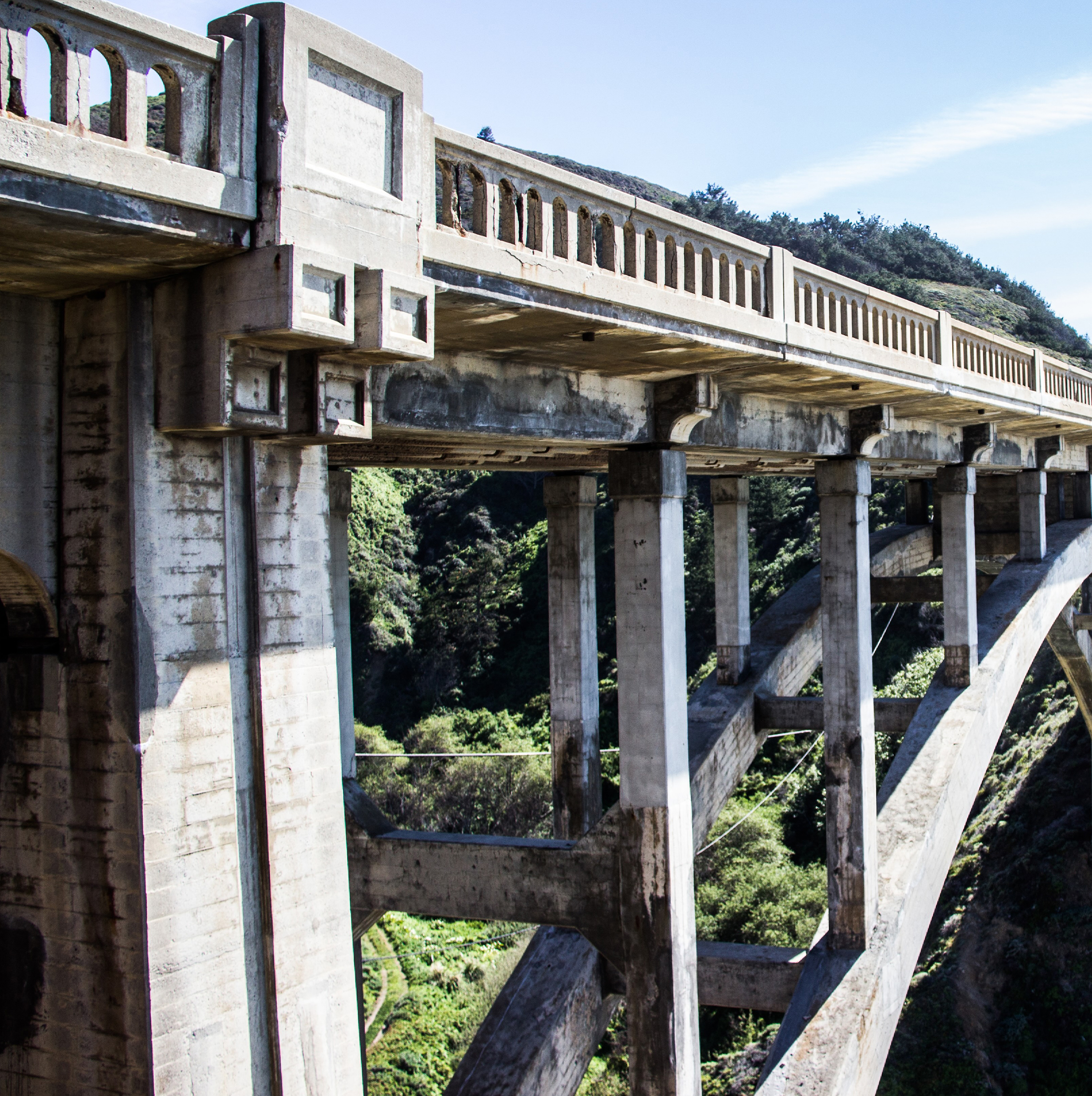 Massive concrete arch supports the bridge over a steep, vegetated gorge
