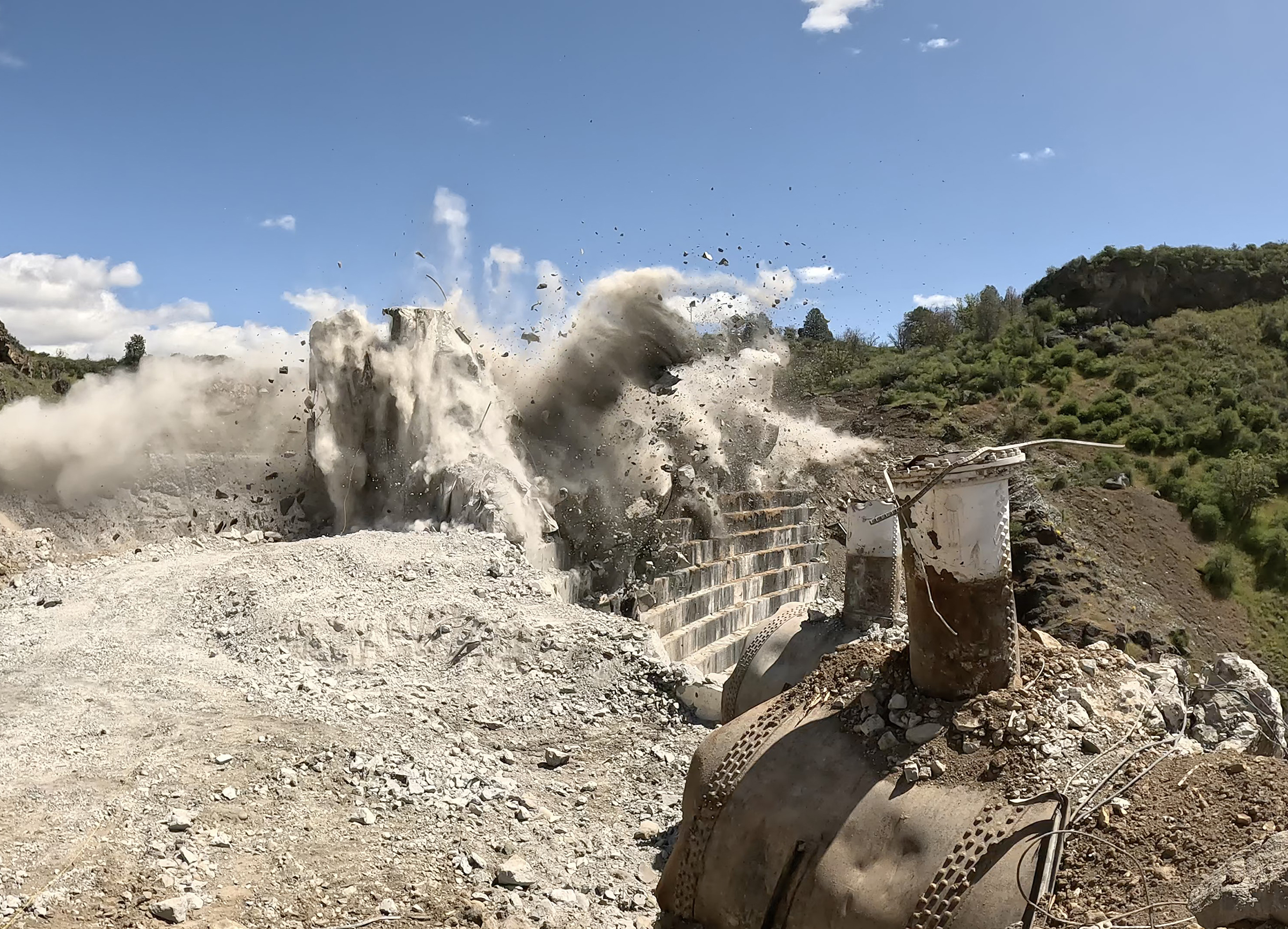 debris flies as a controlled blast takes out part of a dam