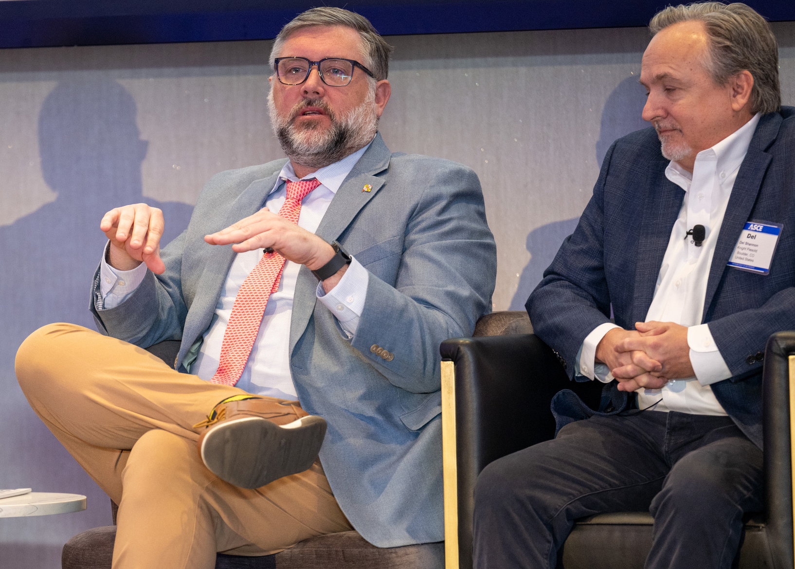 Two men speak onstage, one gesturing while the other listens