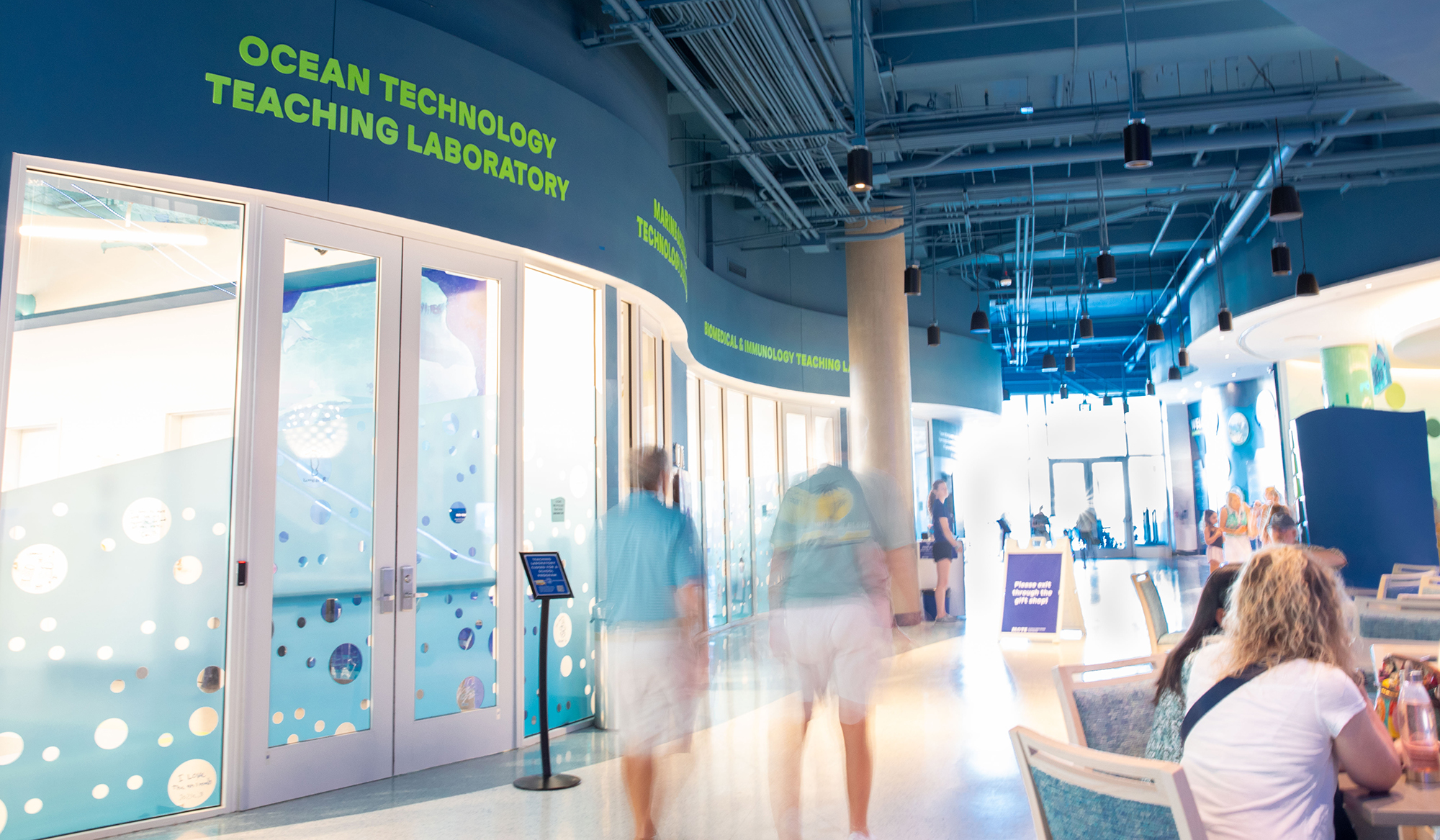 Interior aquarium hallway with ocean technology laboratory, glass walls, and visitors walking