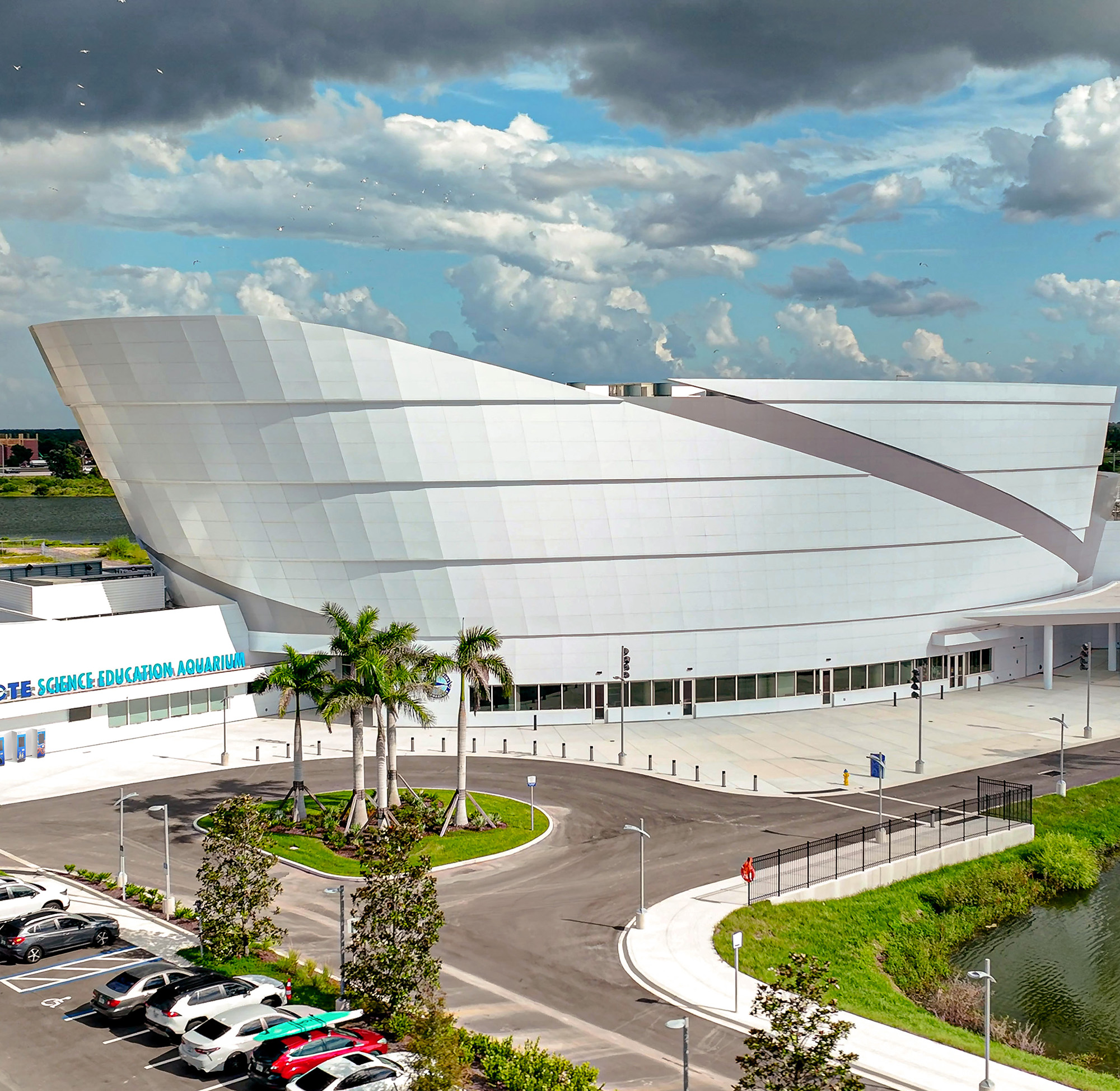 Aerial view of Mote Science Education Aquarium beside water, parking lot, dramatic clouds