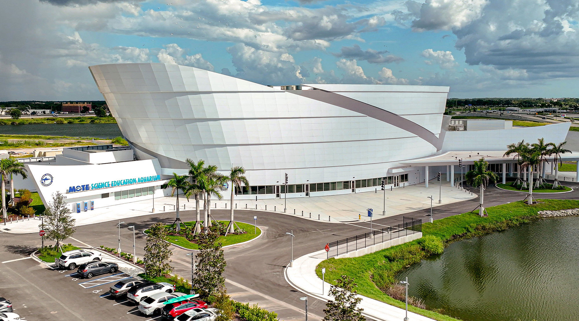 Aerial view of Mote Science Education Aquarium beside water, parking lot, dramatic clouds