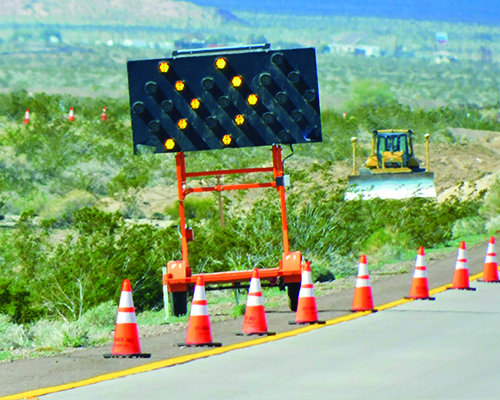 A black directional arrow sign with illuminated yellow lights stands on an orange frame