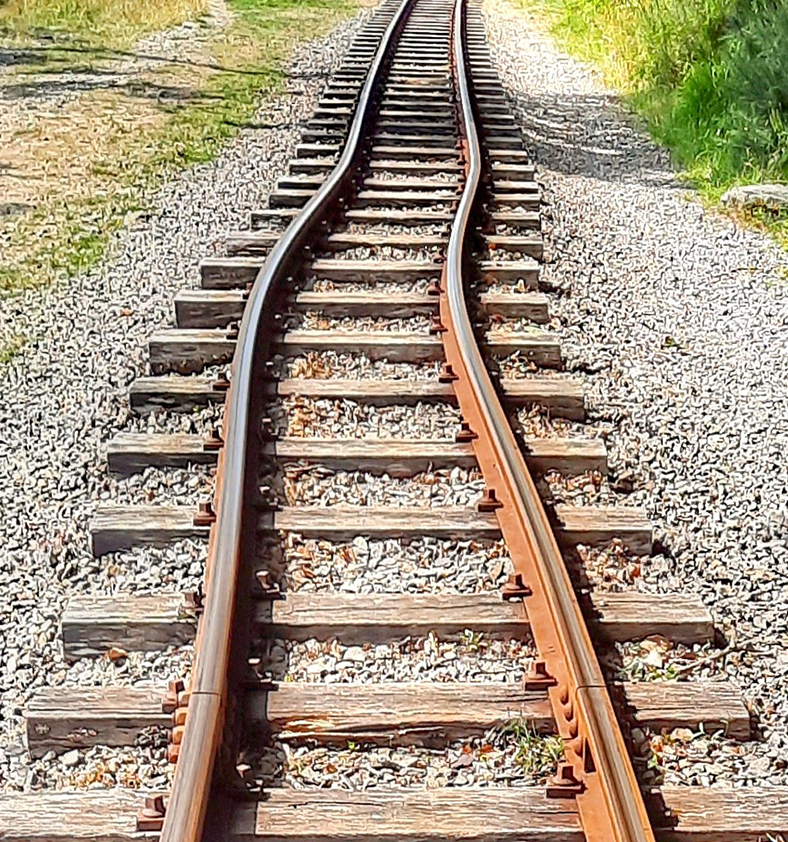Railroad track with pronounced curve running through gravel and grassy surroundings